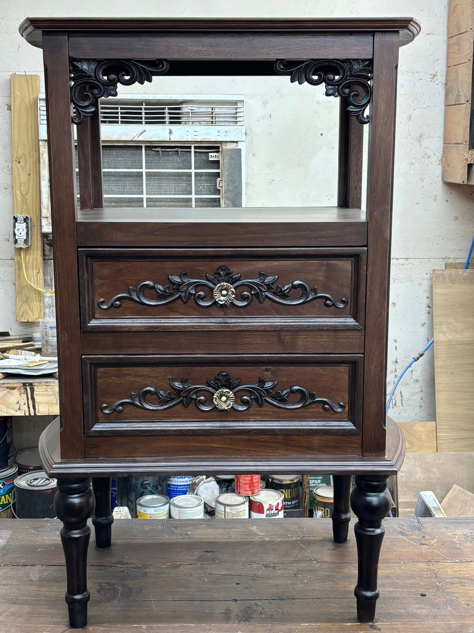 Dark wood cabinet with two drawers and ornate carvings, set on black turned legs.