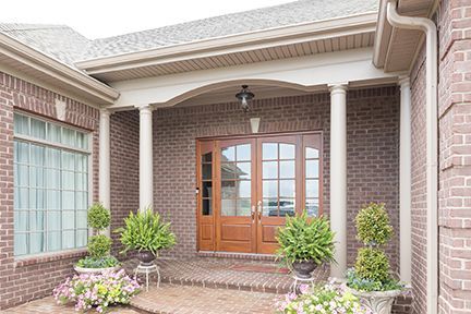 Brick house entrance with double doors, pillars, potted plants, and a covered porch.