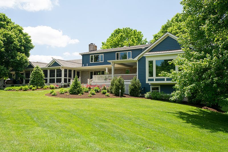Blue house with a large lawn, trees, and a sunny sky.