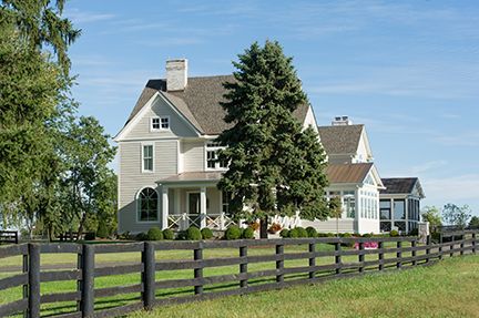 A two-story, light gray house with a black fence, a tree, and blue sky.