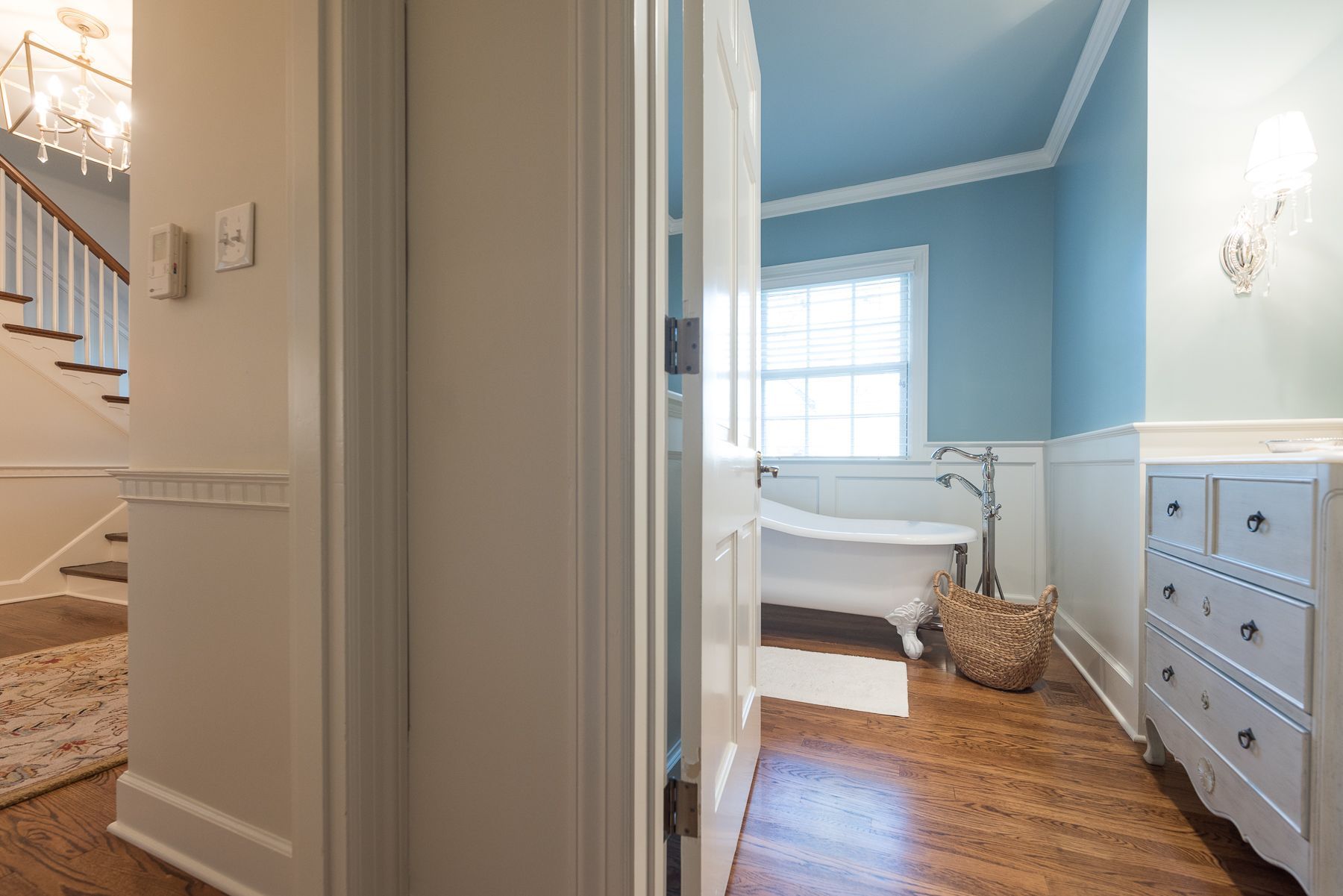 Hallway view: Open door reveals bathroom with clawfoot tub, blue walls, and a dresser.