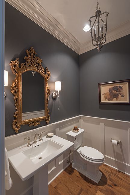 Elegant powder room: gold-framed mirror, pedestal sink, dark gray walls, white wainscoting, and a horse picture.
