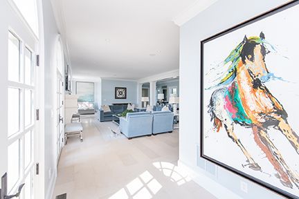 Hallway with white doors, a colorful horse painting, and a living room with blue sofas.