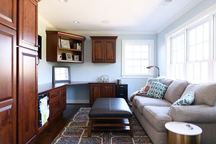 Home office with built-in cabinets, desk, sofa, rug, and ottoman in a room with light blue walls.