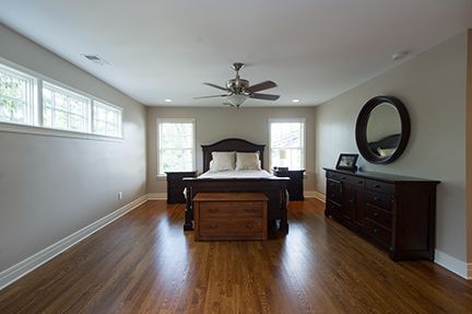 Spacious bedroom with dark wood furniture, hardwood floors, and beige walls.