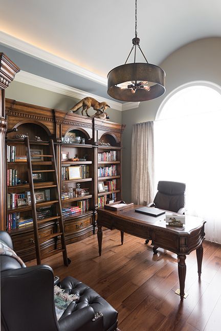 Elegant home office with dark wood bookcase, desk, and leather chair near an arched window.