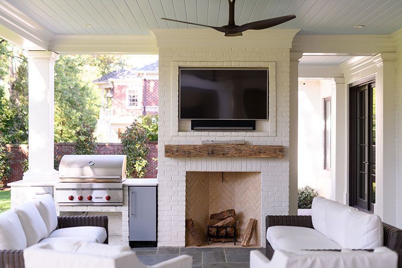 Outdoor living area with fireplace, TV, grill, and white couches.