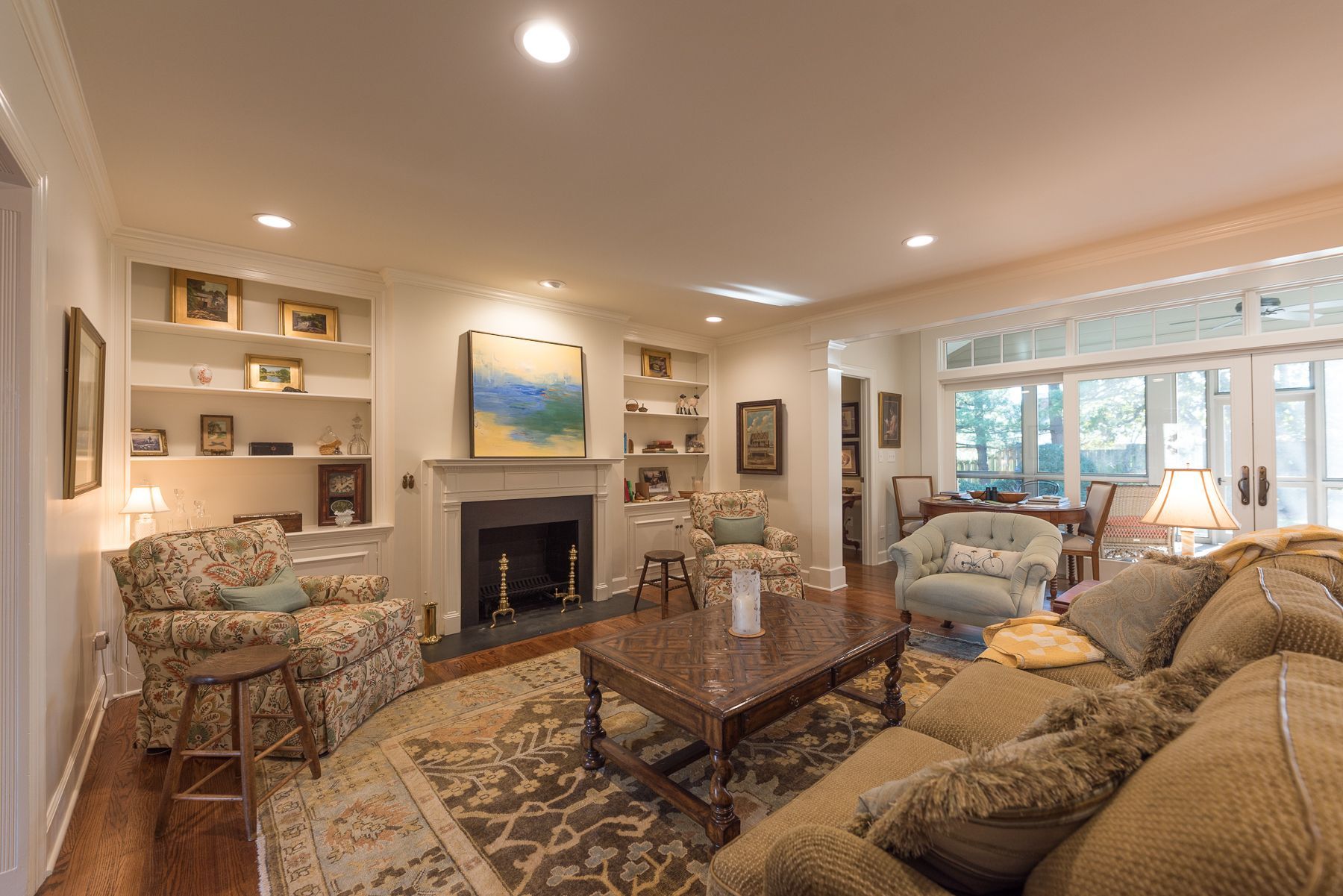 Cozy living room with a fireplace, bookshelves, patterned furniture, and a large window.
