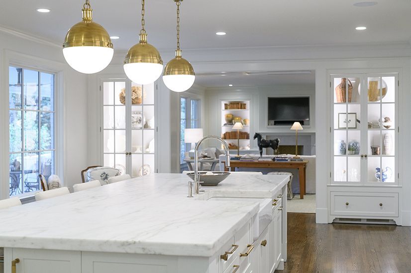 Bright white kitchen with gold pendant lights, marble island, and open doorway to living area.