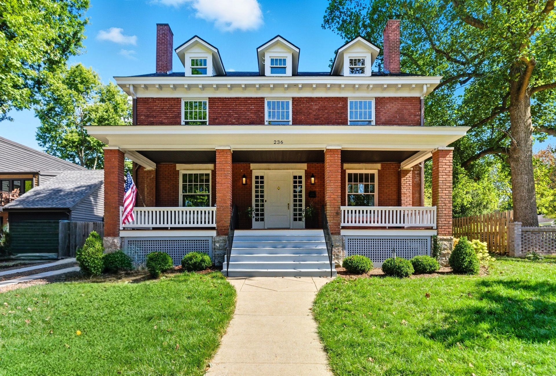 Red brick house with porch, three dormers, and a green lawn.