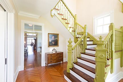 Grand staircase with green banister, hardwood floors, and art in a bright entryway.