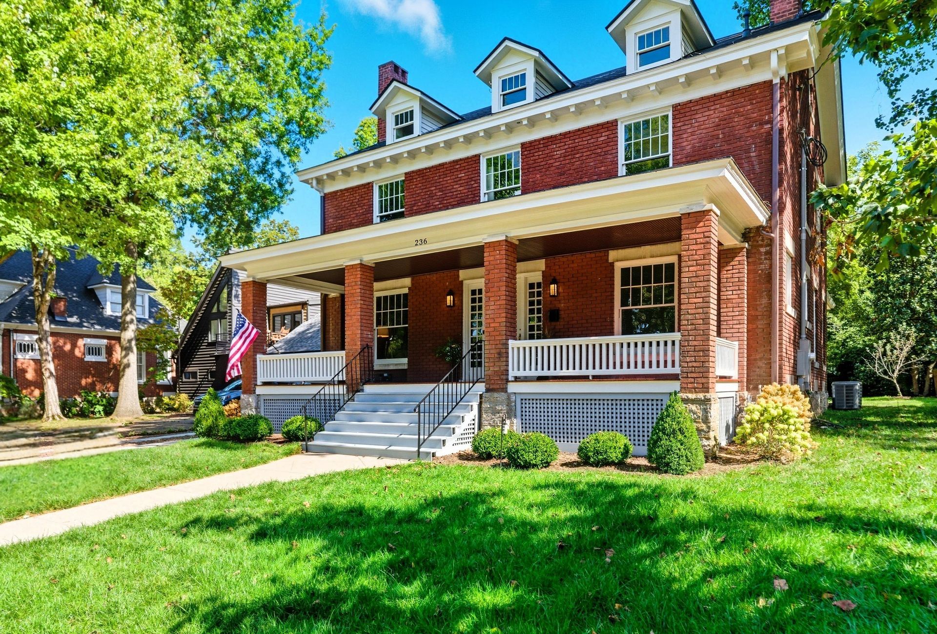 Brick house with white trim, porch, and green lawn under a blue sky.
