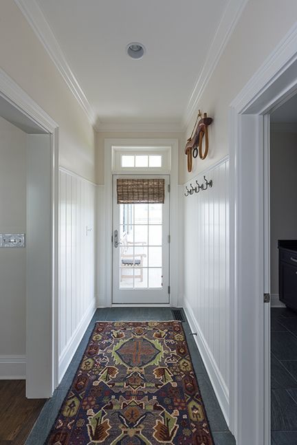 Narrow hallway with patterned rug, beadboard walls, and door with window.