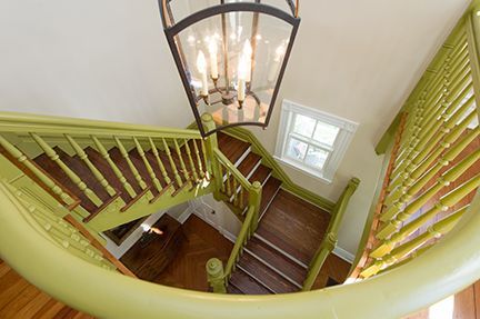 Green staircase with wooden steps, a window, and a hanging chandelier.