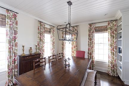 Dining room with a long wooden table, floral curtains, and a chandelier.