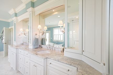 Bright white bathroom with granite countertop, white cabinets, large mirrors, and blue walls.
