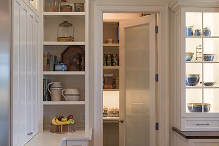 A white kitchen with open shelves, a pantry, and a lit cabinet.