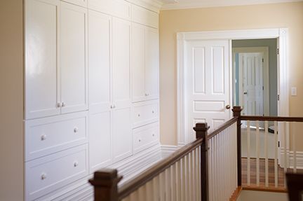 White built-in cabinets line a hallway wall, with a doorway and banister on the right.