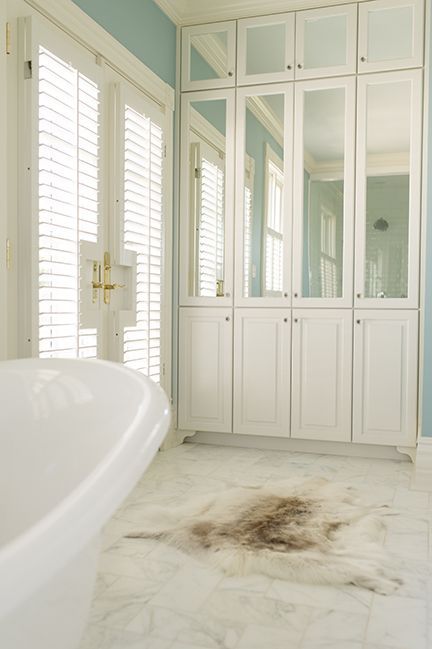 White bathroom with mirrored cabinets, tub, and dirty rug.
