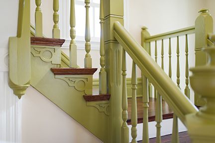 Green painted staircase with ornate balusters, dark brown steps, and a white wall.