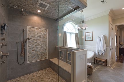 Spacious modern bathroom with walk-in shower, bench, and tub. Gray tile, glass enclosure, and chandelier.