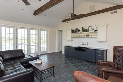 Spacious living room with dark blue cabinets, French doors, leather furniture, and a wood beamed ceiling.