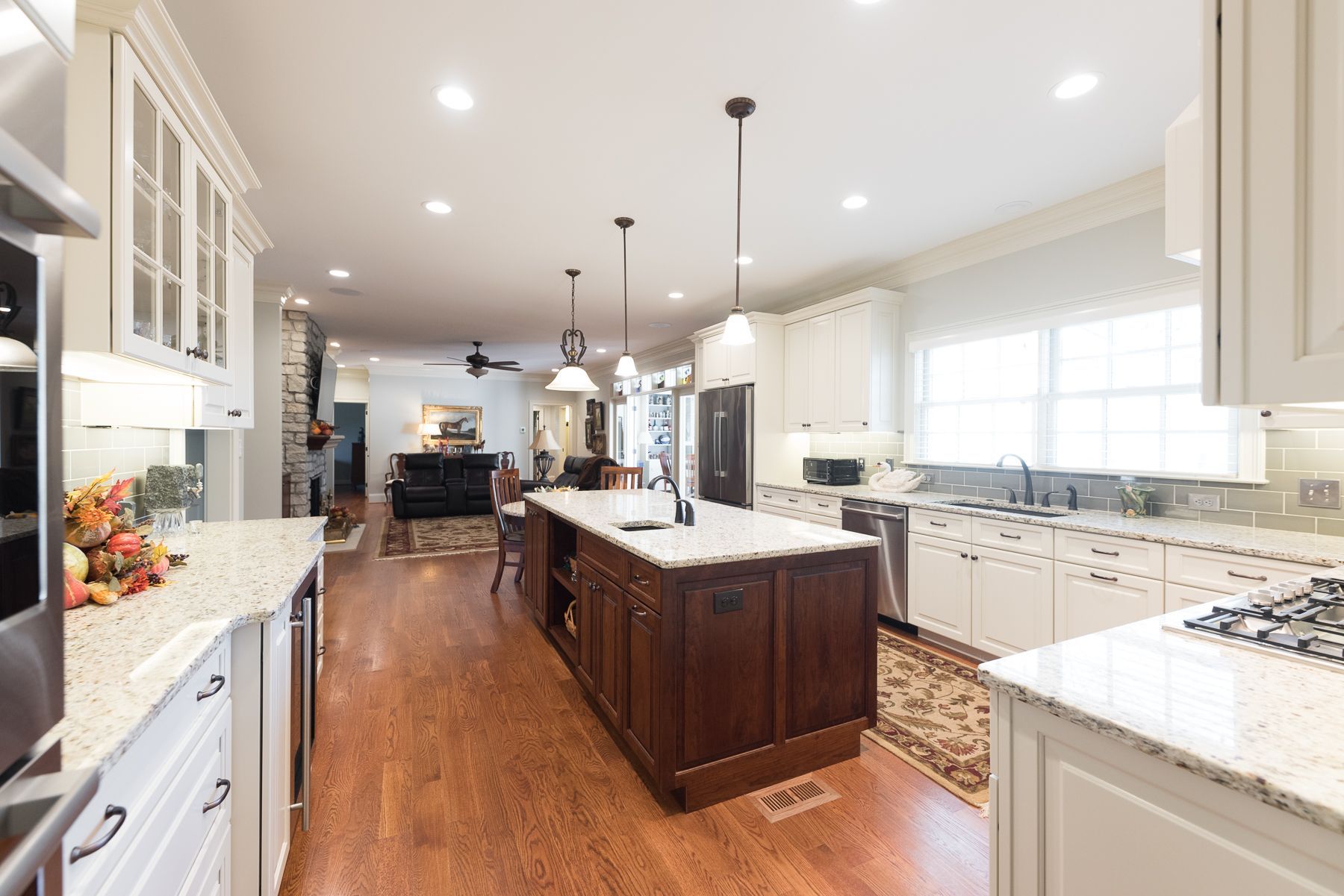 Spacious kitchen with white cabinets, granite countertops, wooden island, and view of a living room.