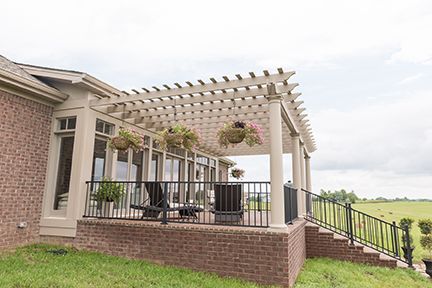 Brick patio with pergola, chairs, and hanging baskets. Overlooks a green field.