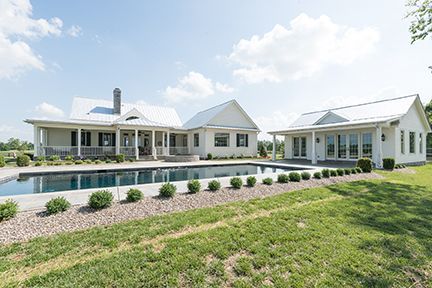 White farmhouse with pool, grassy lawn, blue sky.