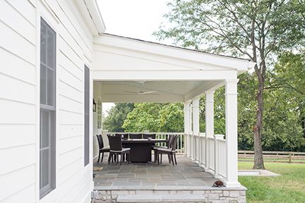 White house with covered porch, outdoor seating, and green yard.