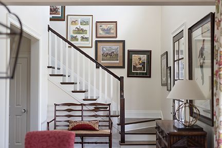 A bright stairwell with art, bench, and table. White walls, brown staircase, and red accents create a warm, inviting space.