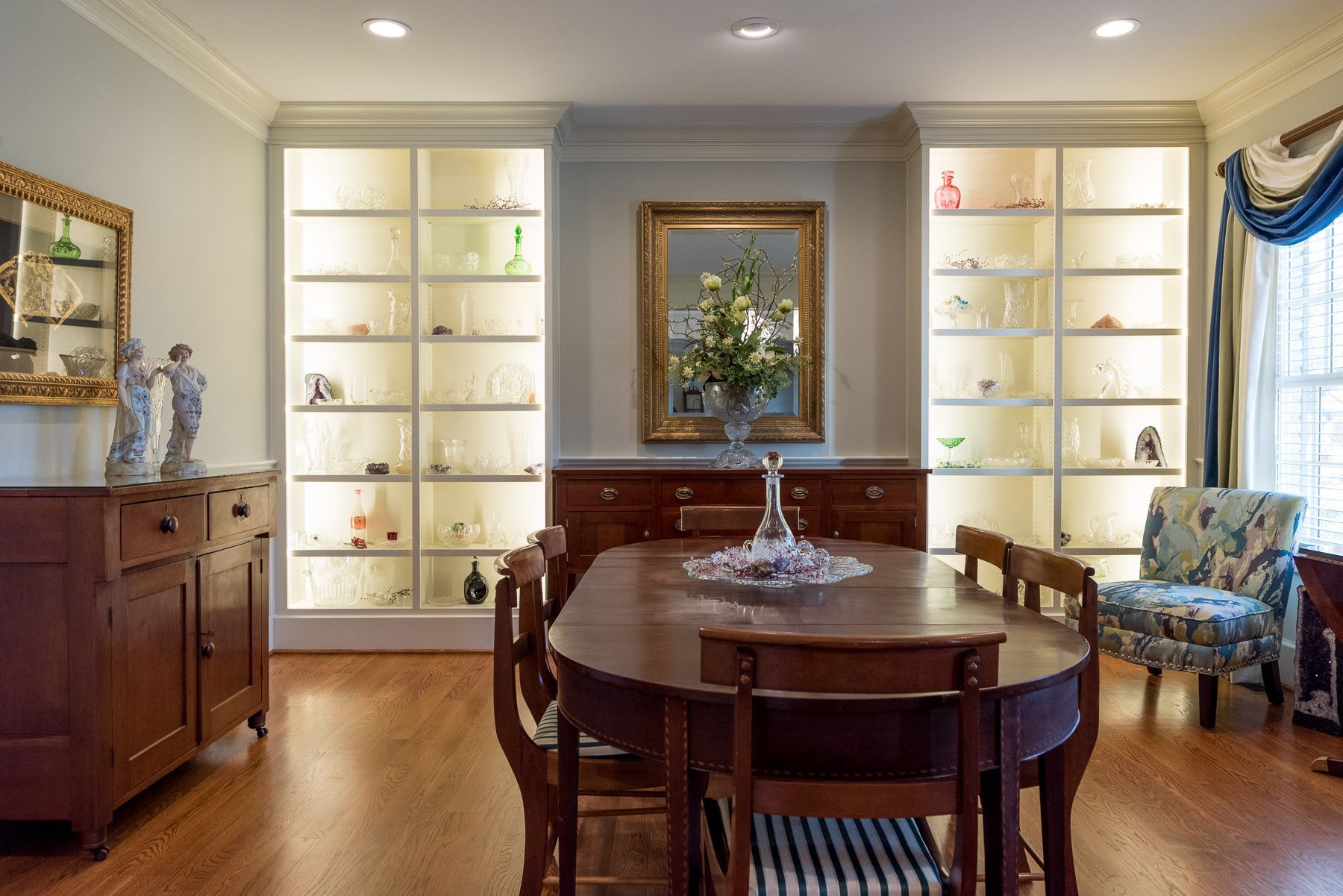 Elegant dining room: wooden table with chairs, illuminated display cabinets, antique furniture, a mirror.