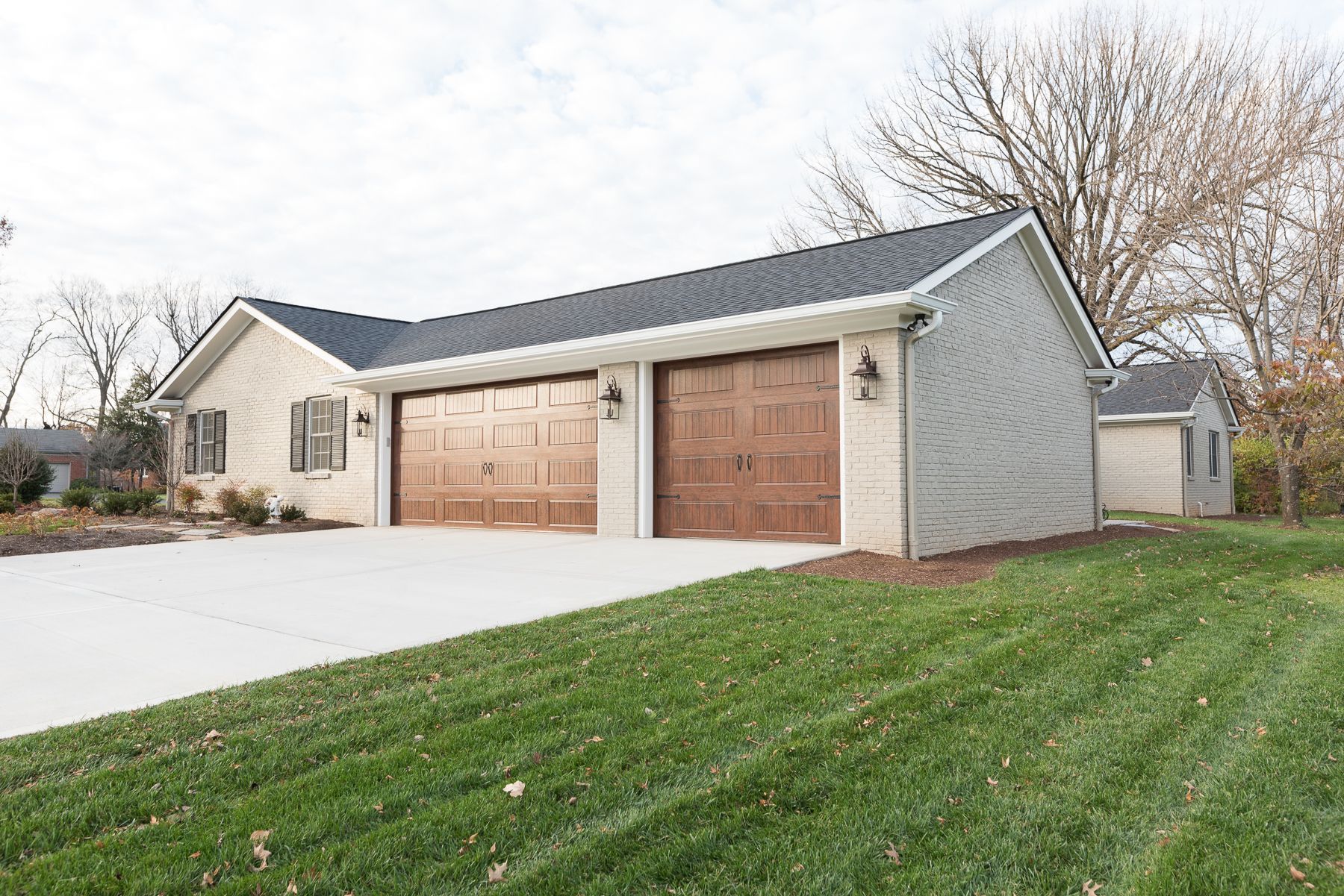 Beige house with two brown garage doors on a concrete driveway, with green lawn.