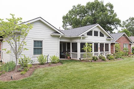 White house with screened porch, green lawn, and landscaping.
