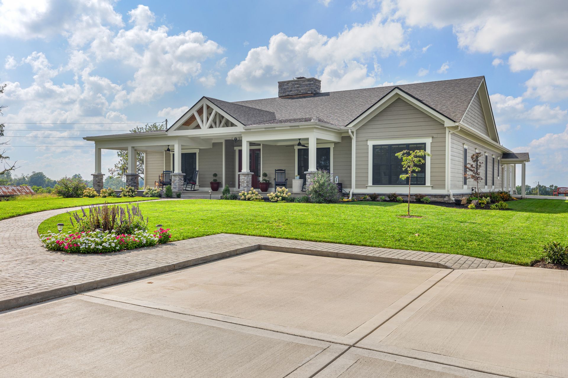 A light green farmhouse with a porch, gray roof, and lush green lawn, blue sky.