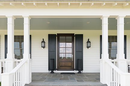 White-columned porch with a brown door, black shutters, and gray stone flooring.