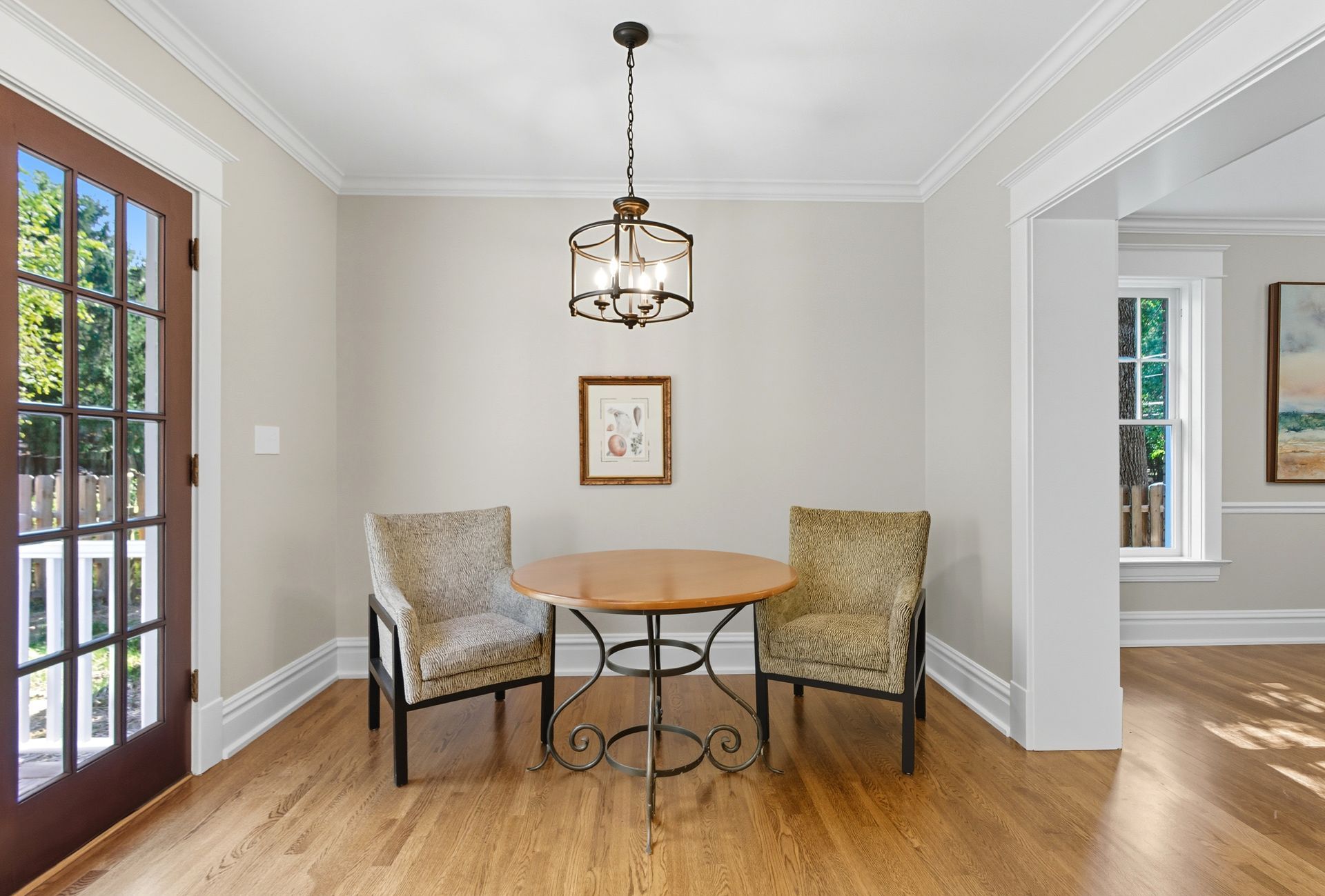 Small dining area with round table, two patterned chairs, framed art, and hanging light fixture.