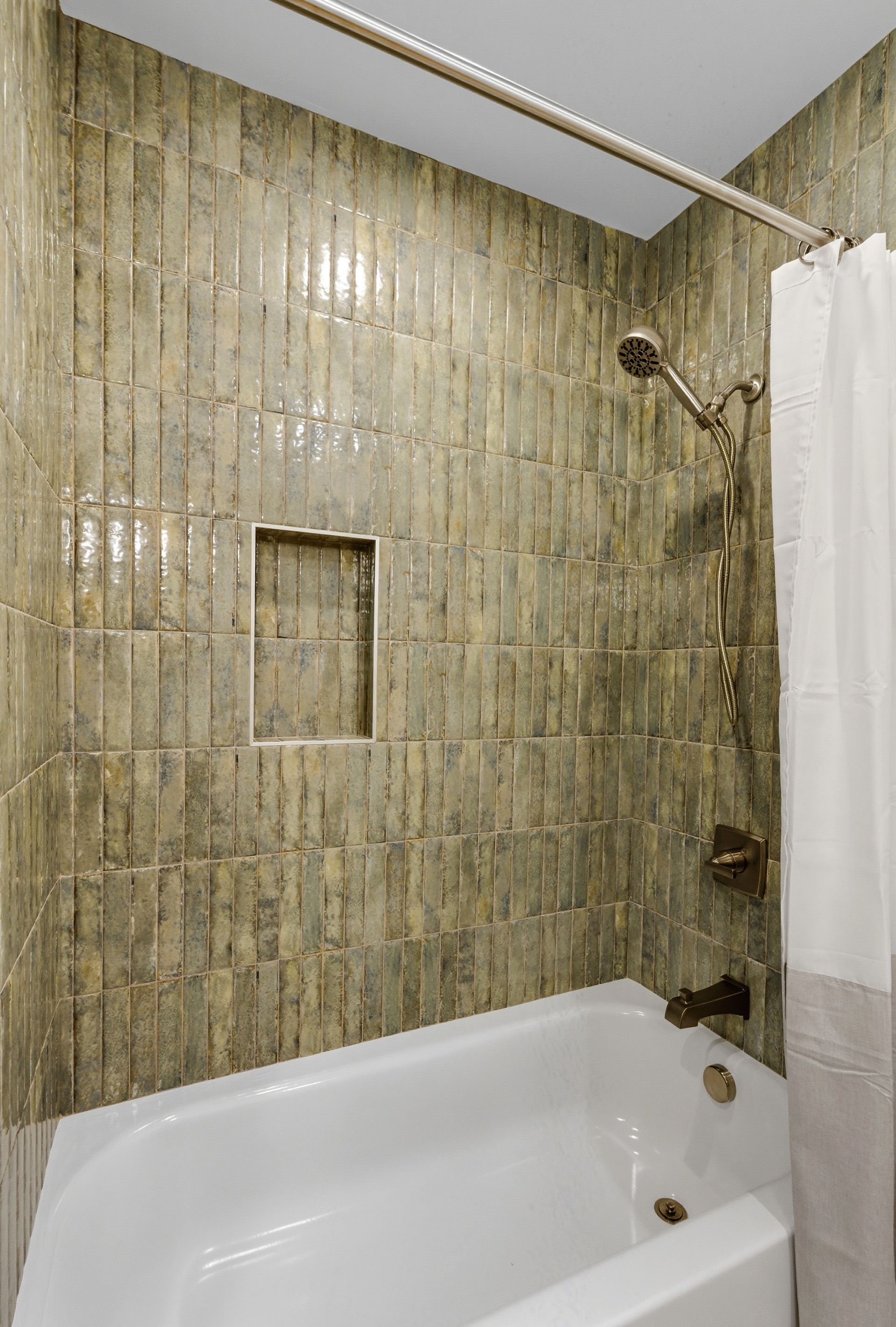 Green tiled shower with built-in shelf, white tub, bronze fixtures, and a curtain.