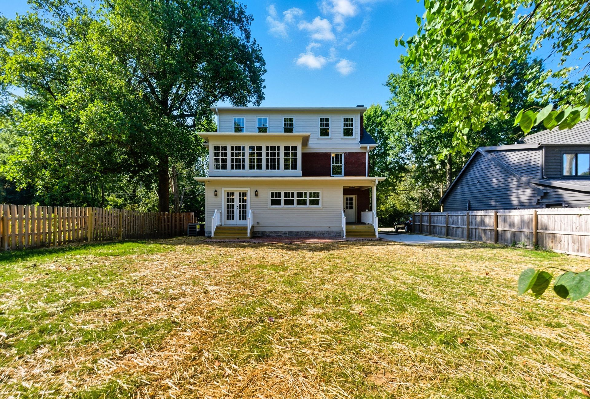 Back view of a three-story house with a spacious yard and wooden fence.