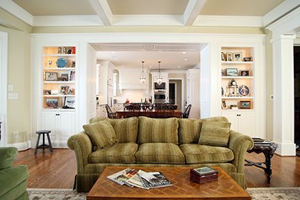 Living room with green sofa, built-in bookshelves, and view into the kitchen. Wooden floors and coffee table.
