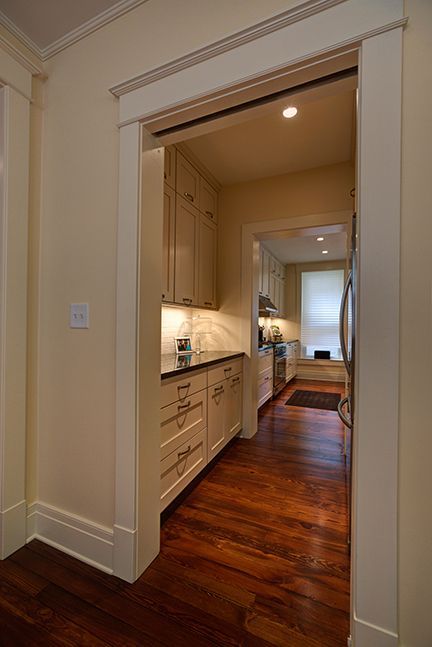 Narrow kitchen hallway with light cabinets, dark wood floor, and a glimpse of a stovetop.