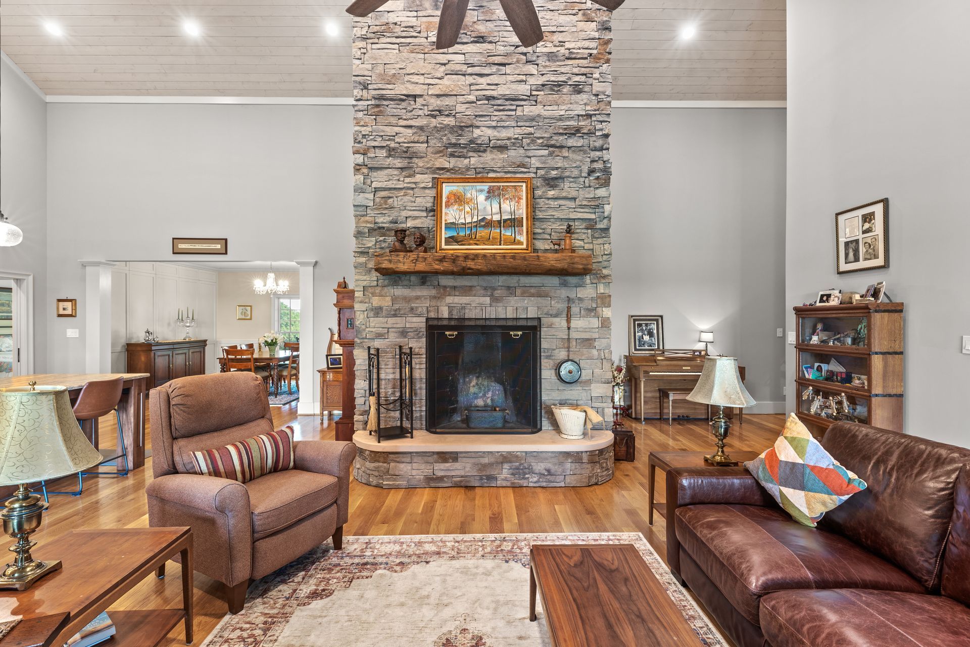 Living room with stone fireplace, brown leather furniture, and hardwood floors.