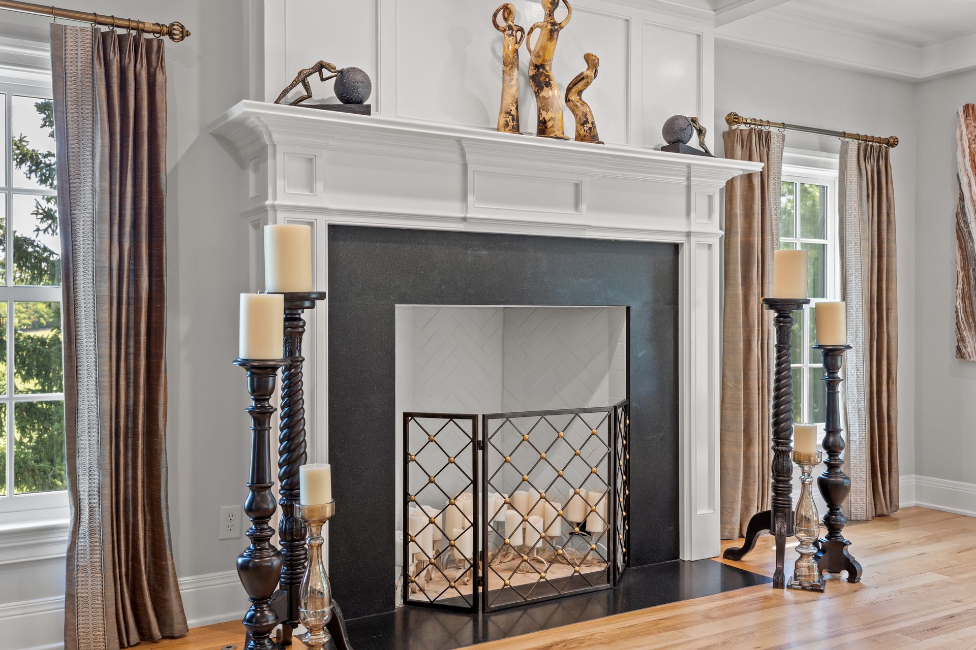Fireplace with candles, wooden floor.  Grey walls, white trim. Brown curtains, decor on mantel.