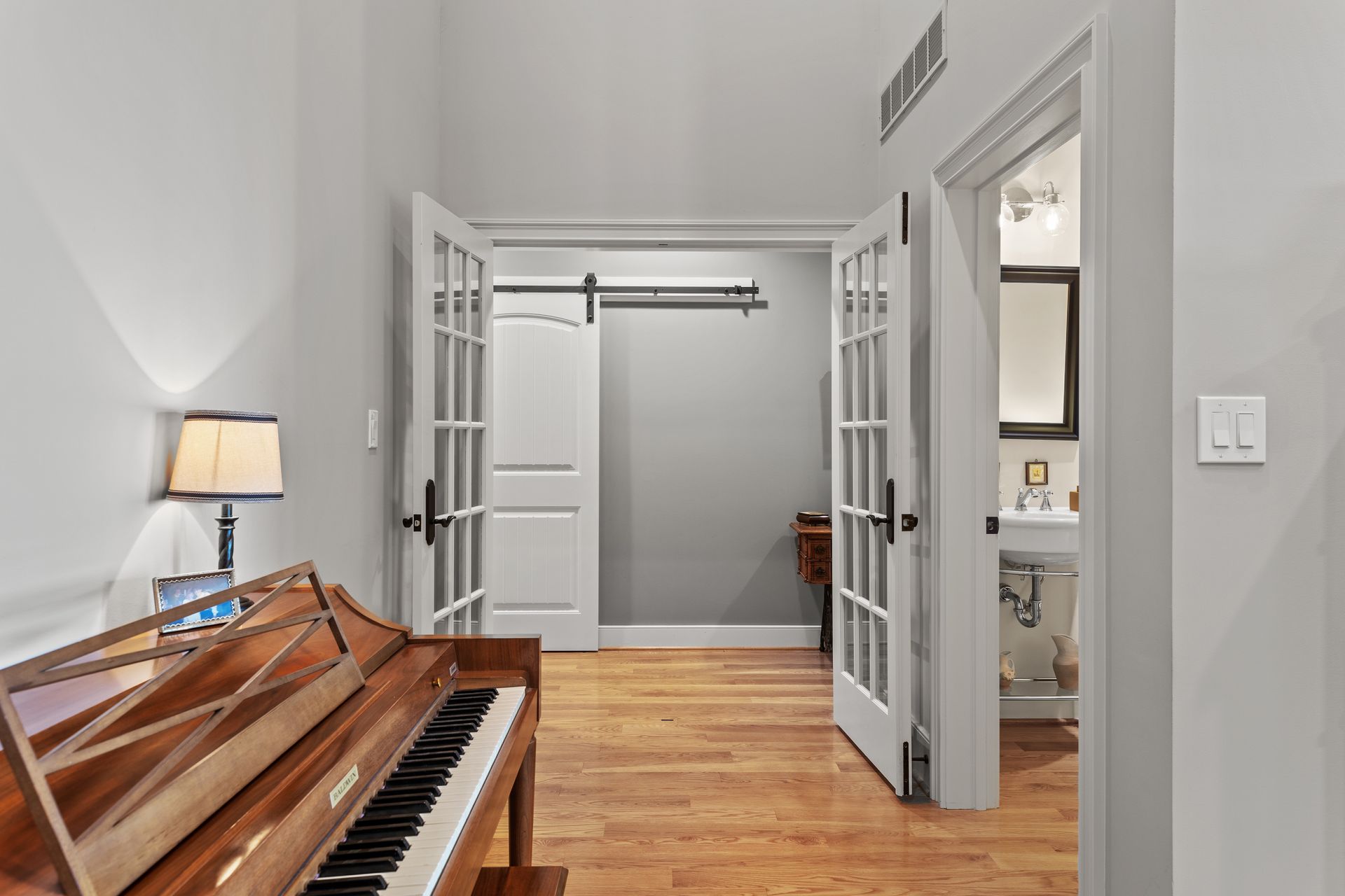 Hallway with piano, open doors to a closet and bathroom, hardwood floors.