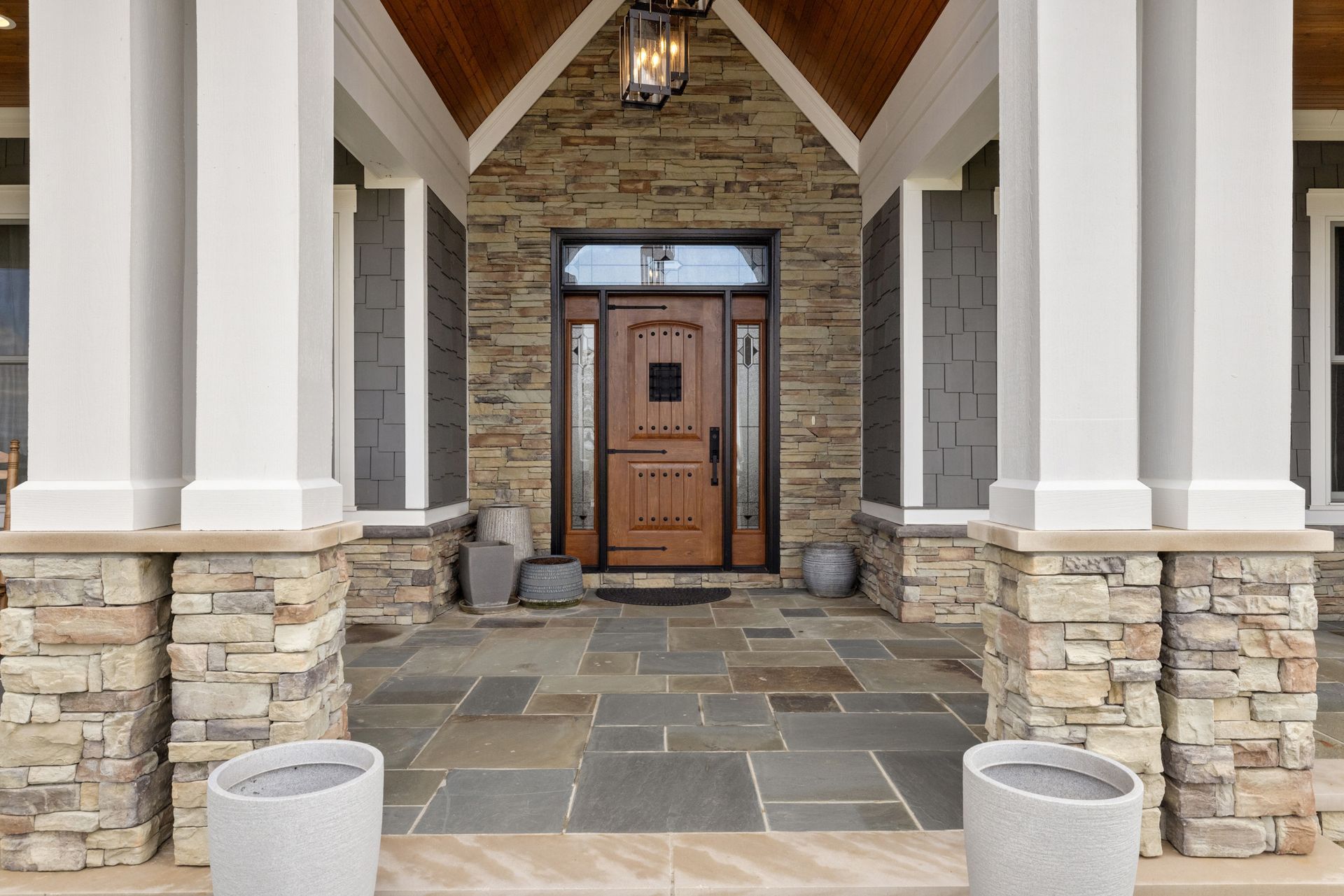 Front porch with stone columns, wooden door, and stone flooring.