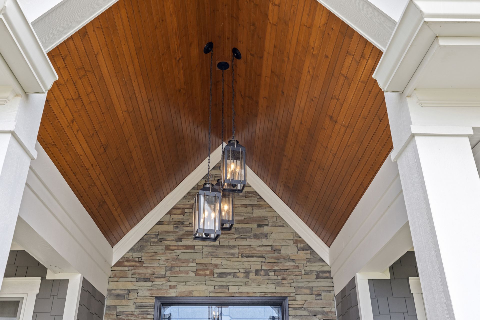 Wooden ceiling entryway with stone wall, white pillars, and hanging lanterns.