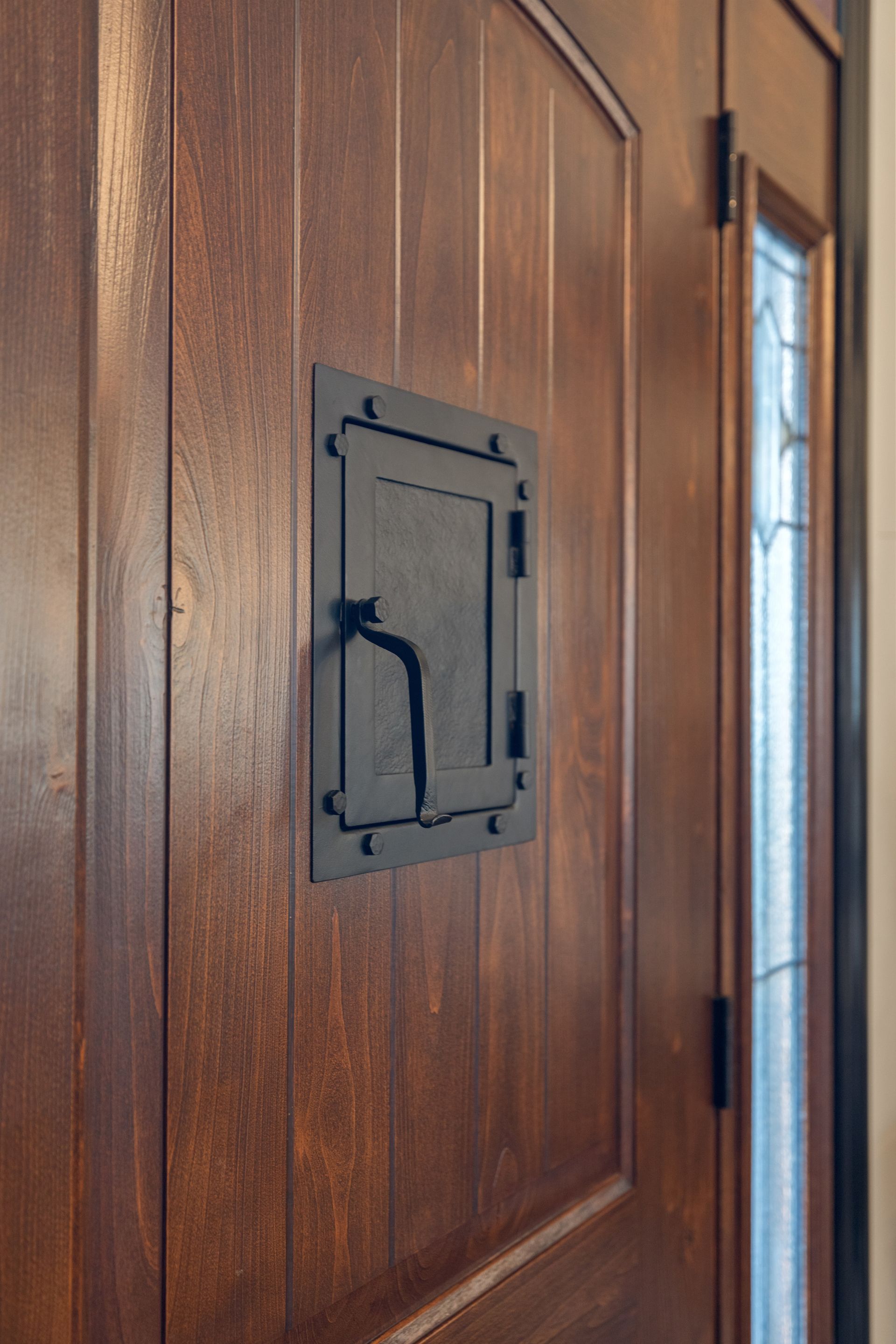 Wooden door with a small, black, square, mail slot.