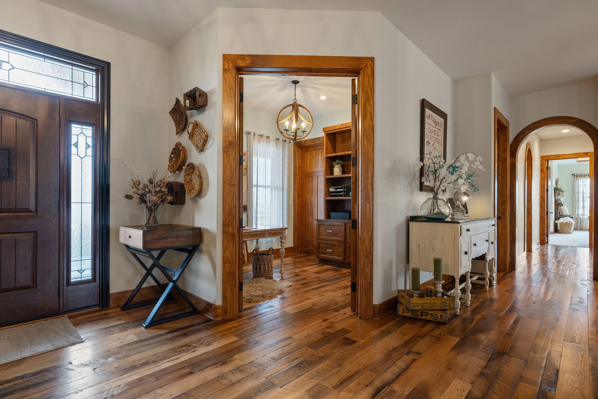 Entryway with wooden floors, a front door, and doorways leading to other rooms; a console table and decor are present.