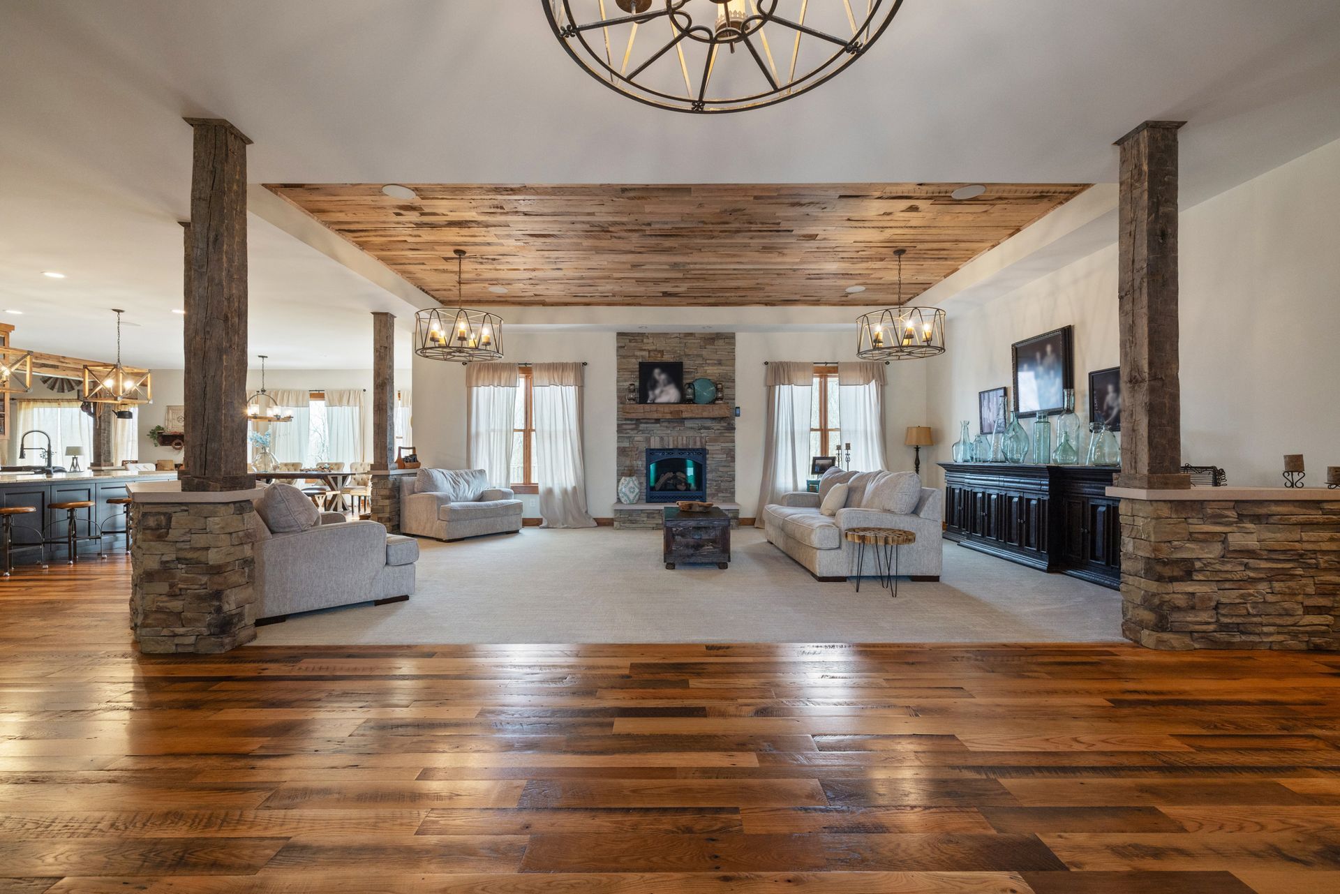 Spacious living room with stone pillars, wood ceiling, fireplace, and hardwood floors.
