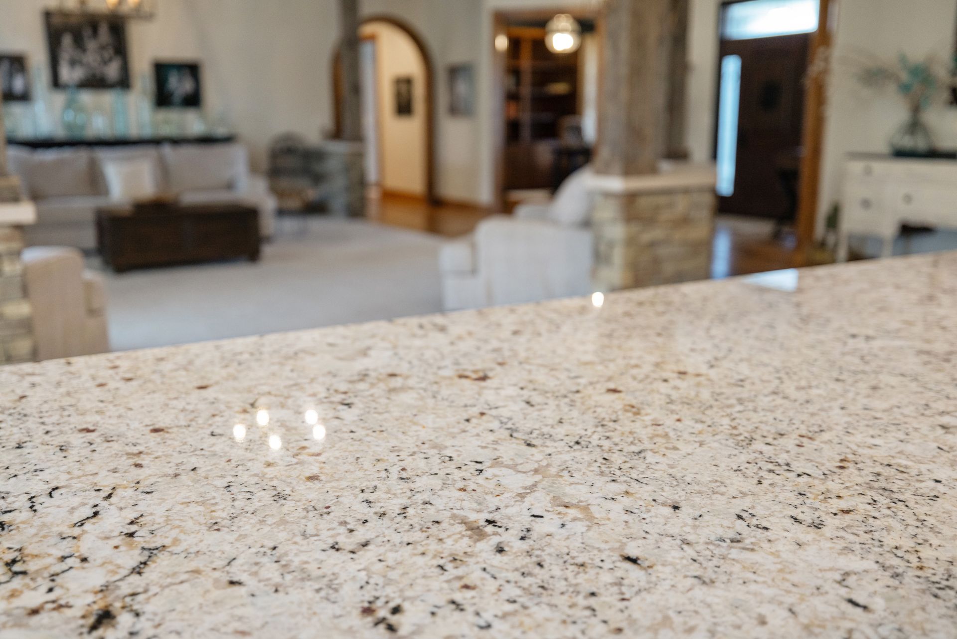 Close-up of a light-colored granite countertop with a blurred living room in the background.